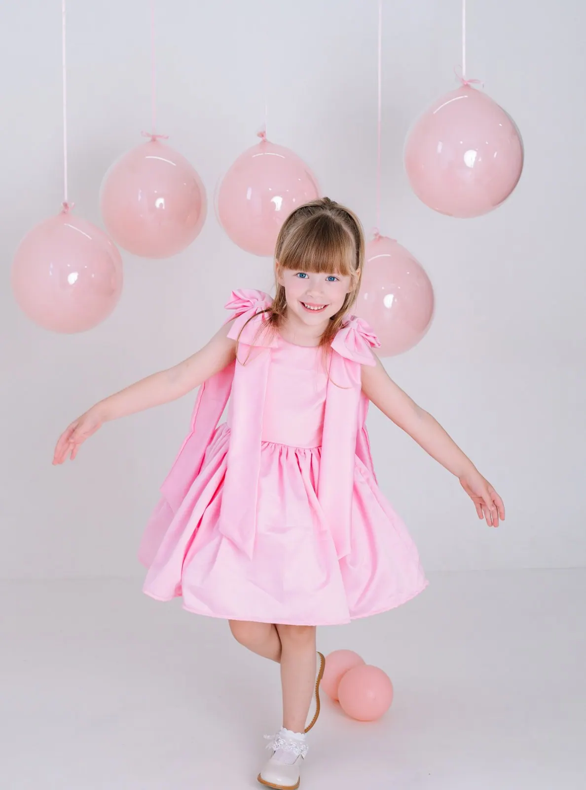 Menina de vestido rosa gira sorrindo entre balões rosa pendurados