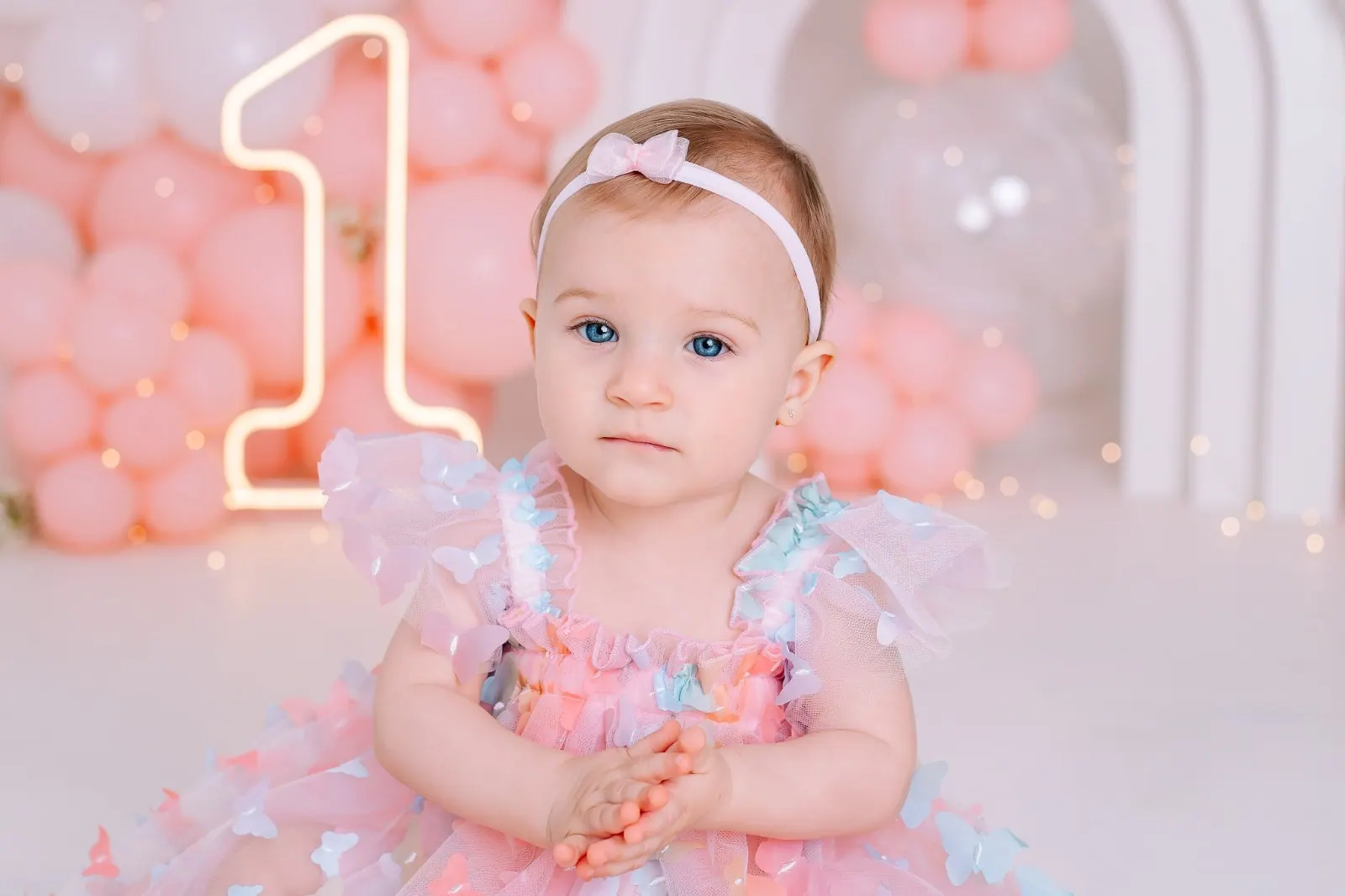 Bebê de olhos azuis com vestido de borboletas no ensaio de um ano