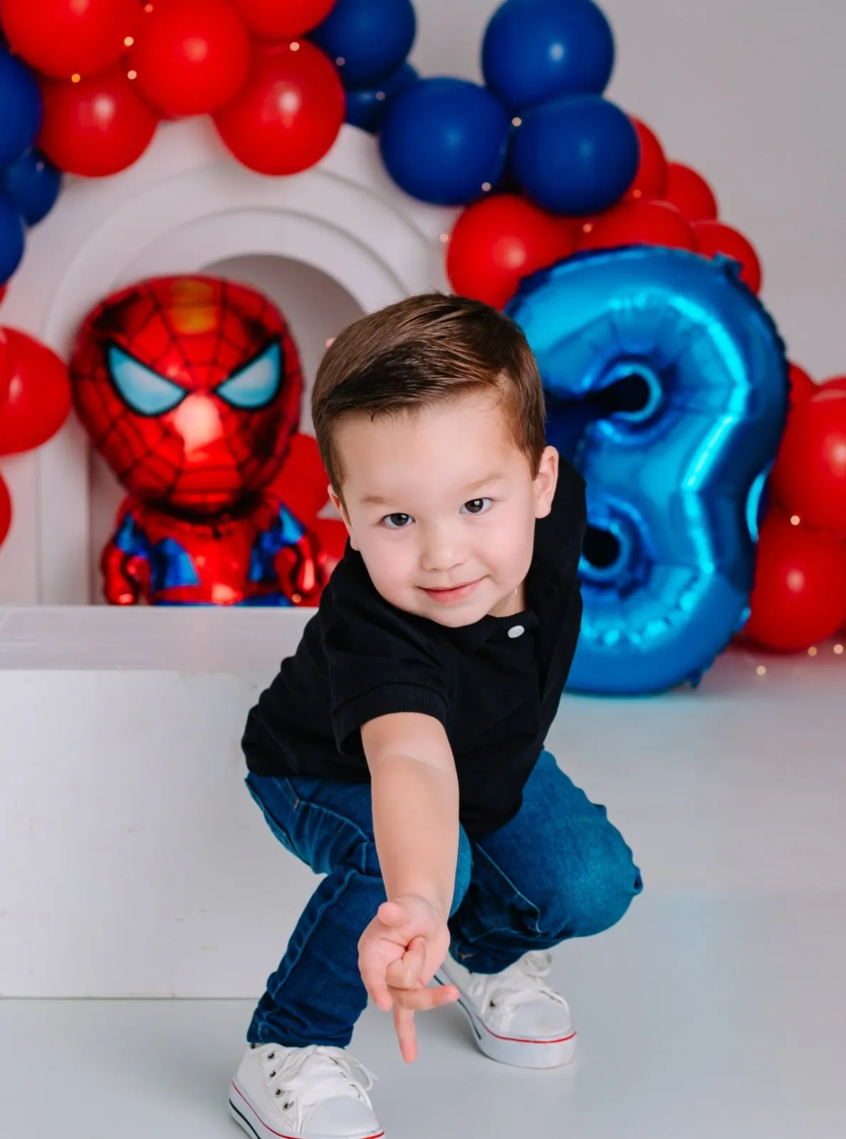Menino de três anos faz pose de super-herói diante de balões vermelhos e azuis