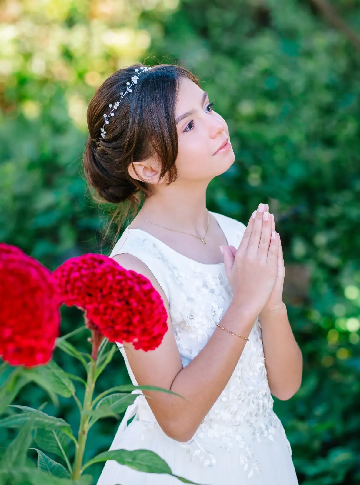 Menina de vestido branco de primeira comunhão com as mãos em oração entre flores vermelhas