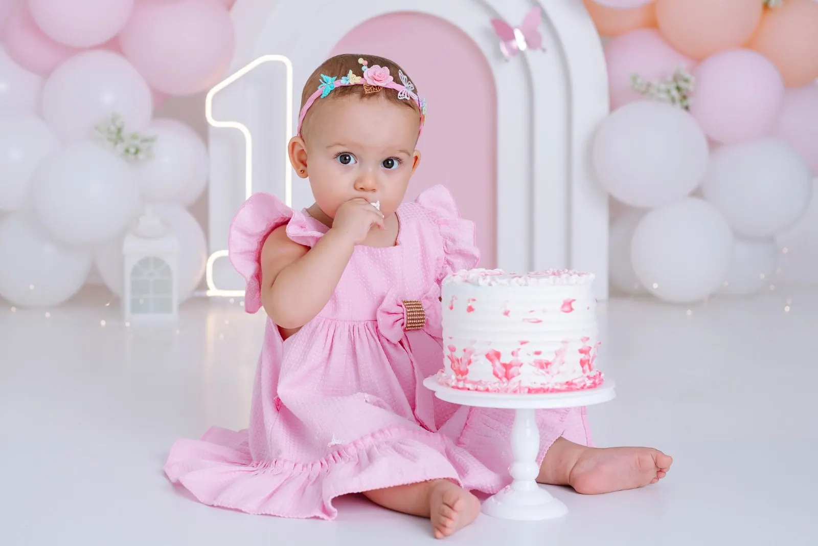 Bebê de vestido rosa prova o bolo no ensaio smash the cake de um ano